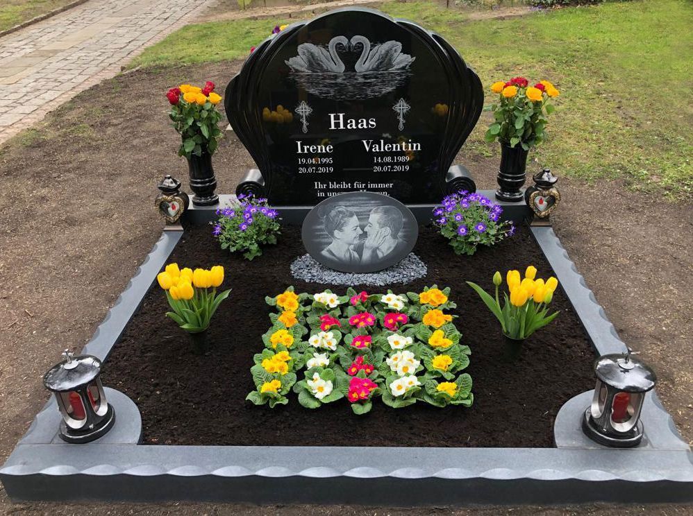 Gedenkgrab mit schwarzem Grabstein, Blumen und Kerzenlaternen in einem ordentlich eingefassten Gartengrundstück