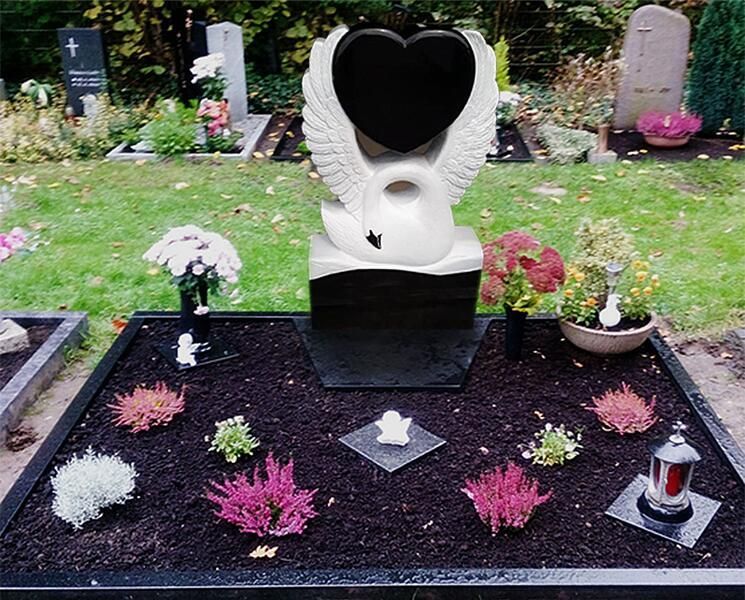 Gedenkgrab mit weißer Engelsstatue, schwarzem Grabstein und rosa und weißen Blumen auf einem Friedhof