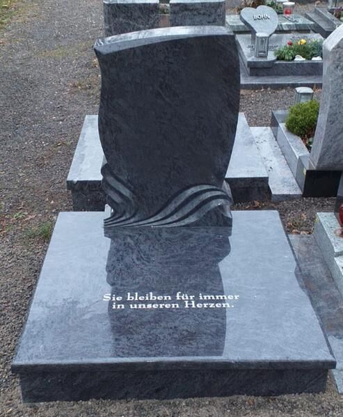 Schwarzer Granitgrabstein mit Wellenmotiv und weißer Inschrift auf einem Friedhof
