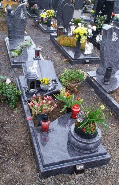 Grab mit Topfblumen und Kerzen auf einem Friedhof, umgeben von dunklen Steinmarkierungen.