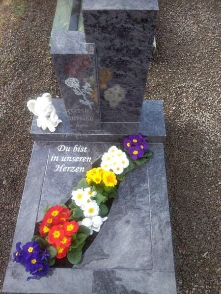 Grabstein mit Blumen und einem weißen Teddybären zum Gedenken