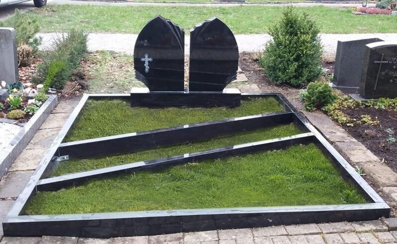 Moderne Grabstätte mit zwei schwarzen Grabsteinen und einem dreieckigen grünen Rasenbeet