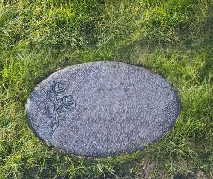 Ovale graue Steintafel mit floralen Schnitzereien, eingefasst in grünes Gras
