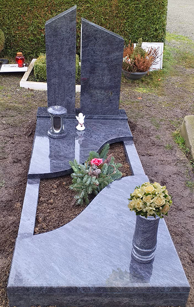 Moderner Grabstein aus Granit mit zwei aufrechten schwarzen Gedenktafeln und Blumentöpfen in einem Friedhofsgartenbereich