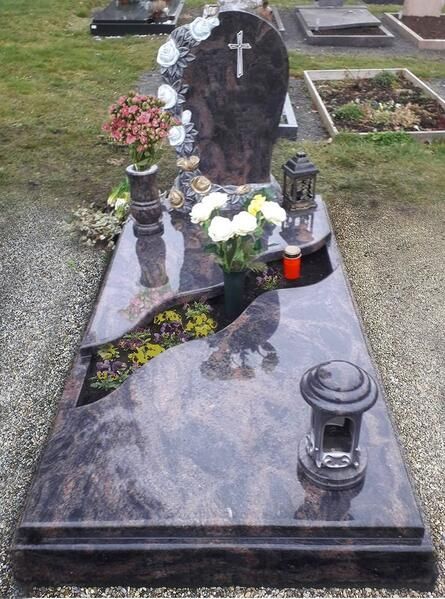 Schwarzer Granitgrabstein mit weißem Kreuz, Blumen, Laternen und Kerzen auf einem Friedhof