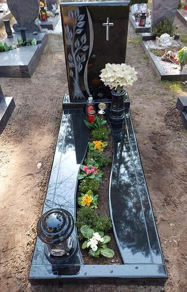 Grab aus schwarzem Granit mit weißen Blumen und roten Kerzen auf einem Friedhof