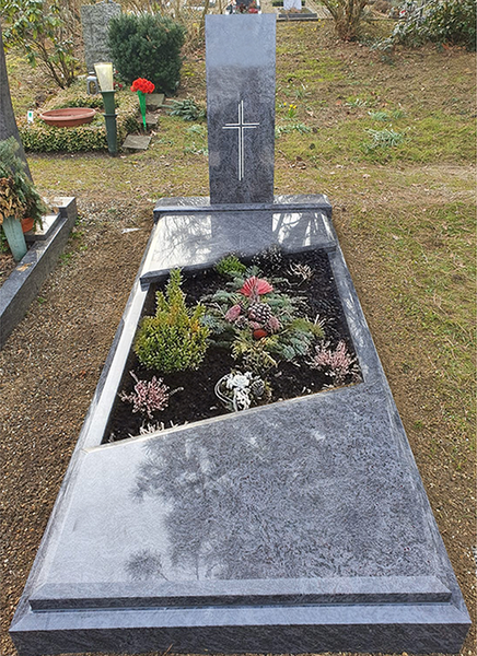 Grabstein mit Kreuz und Blumenbeet als Gedenkstein auf einem Friedhof