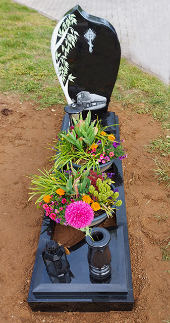 Grabstein mit bunten Blumen und einer schwarzen Statue auf einem polierten schwarzen Sockel