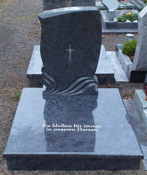 Schwarzer Granitgrabstein mit einem kleinen Kreuz, aufgestellt auf einem Friedhof.