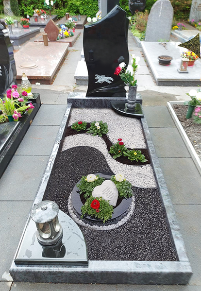 Modernes Grab mit schwarz-weißem Steindesign und kleinen Blumenarrangements auf einem Friedhof