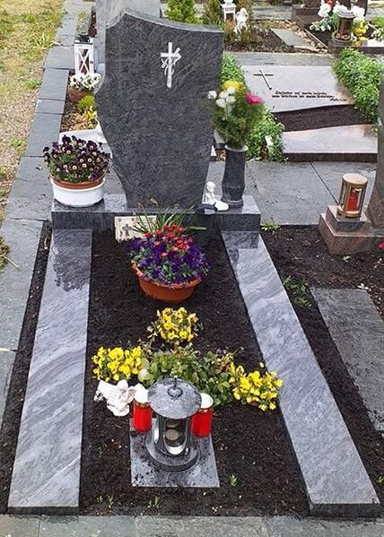 Gedenkgrabstein mit Blumen und Laternen auf einem Friedhof.