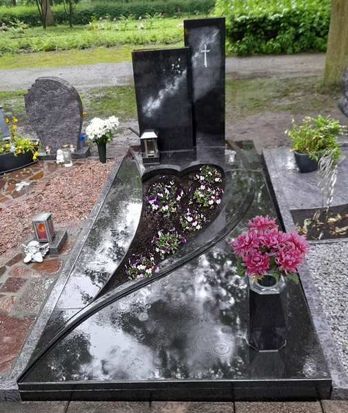 Schwarz poliertes Grab mit herzförmigem Blumenbeet und rosa Blumensträußen auf einem Friedhof