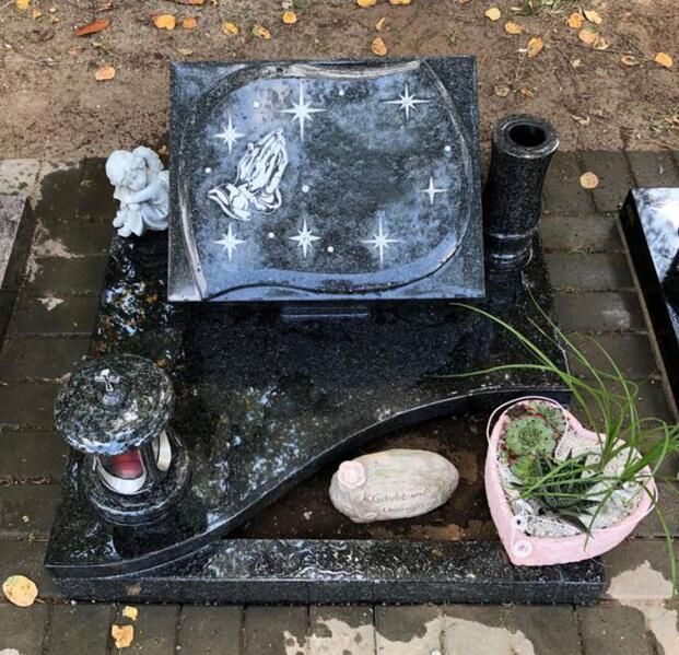 Verzierter schwarzer Grabstein mit Sternen und einem Engel, umgeben von Kerzen und Blumen.