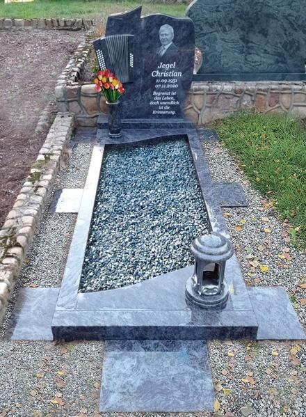 Grabstein mit Blumenstrauß neben einem Kiesgrab und Laterne auf einem Friedhof
