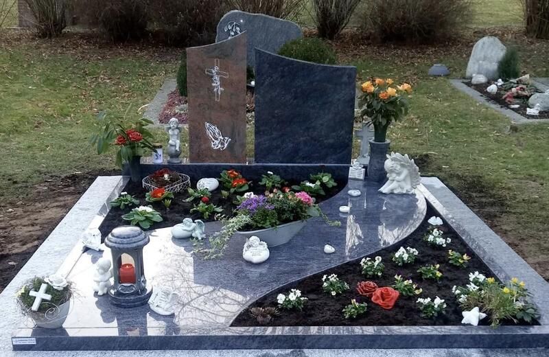Ein geschmücktes Friedhofsgrab mit poliertem schwarzem Grabstein, Blumen, Kerzen und weißen Randfliesen