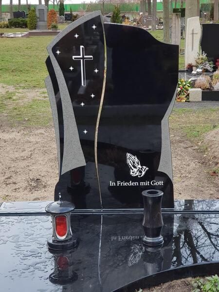 Schwarzer, polierter Granitgrabstein mit Kreuz und weißer Schrift auf einem Friedhof