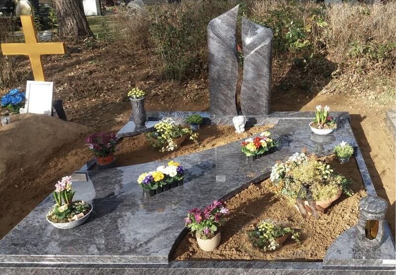 Grabstätte mit Granitgrabstein, Blumen und einem Kreuz auf einem bewaldeten Friedhof