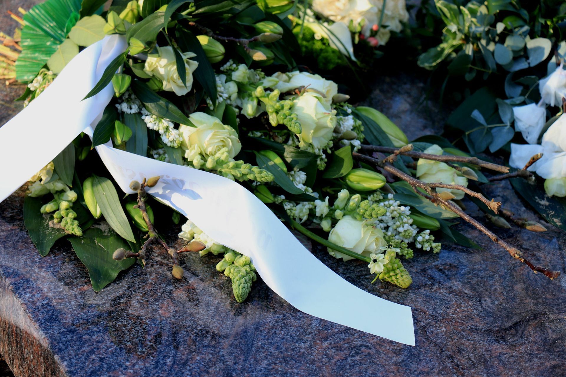 Weißer Blumenstrauß mit grünen Blättern und langen weißen Bändern auf dunklem Steingrund