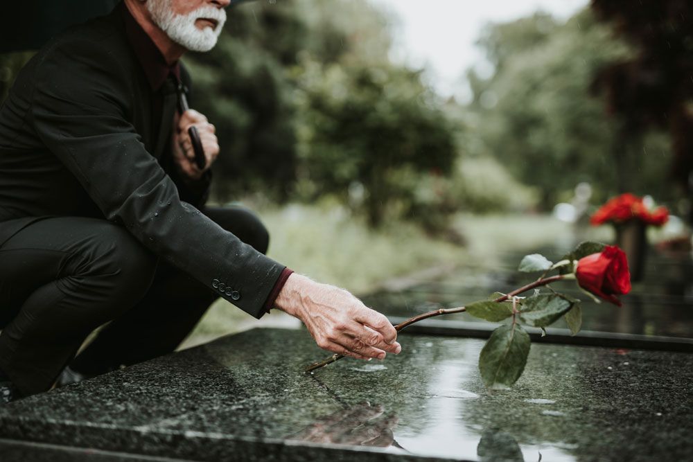 Eine Person legt eine rote Rose auf einen polierten Grabstein auf einem Friedhof.