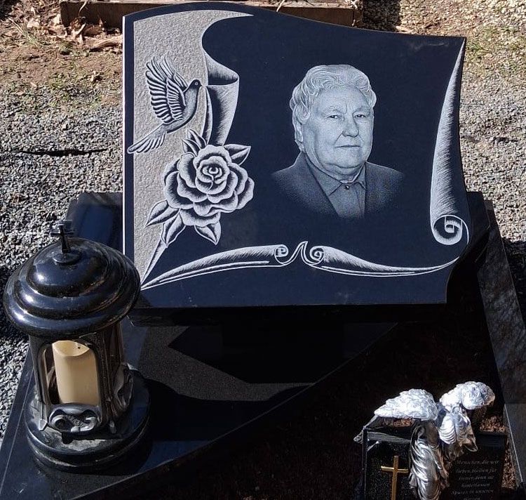 Schwarzer Granitgrabstein in einem Garten, mit einer Porträtgravur und weißer Inschrift auf der rechten Seite