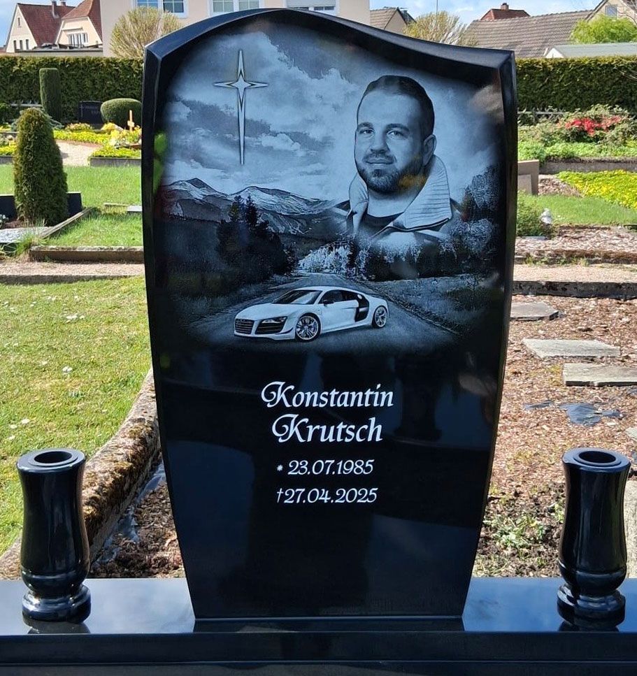 Schwarzer Gedenkgrabstein mit Porträt, Kreuz und Auto-Gravur auf einem Friedhof