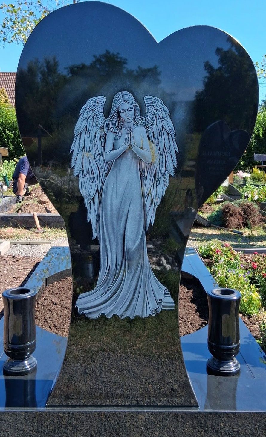 Schwarze, herzförmige Engel-Gedenkstatue in einem Garten, mit zwei schwarzen Vasen an den Seiten