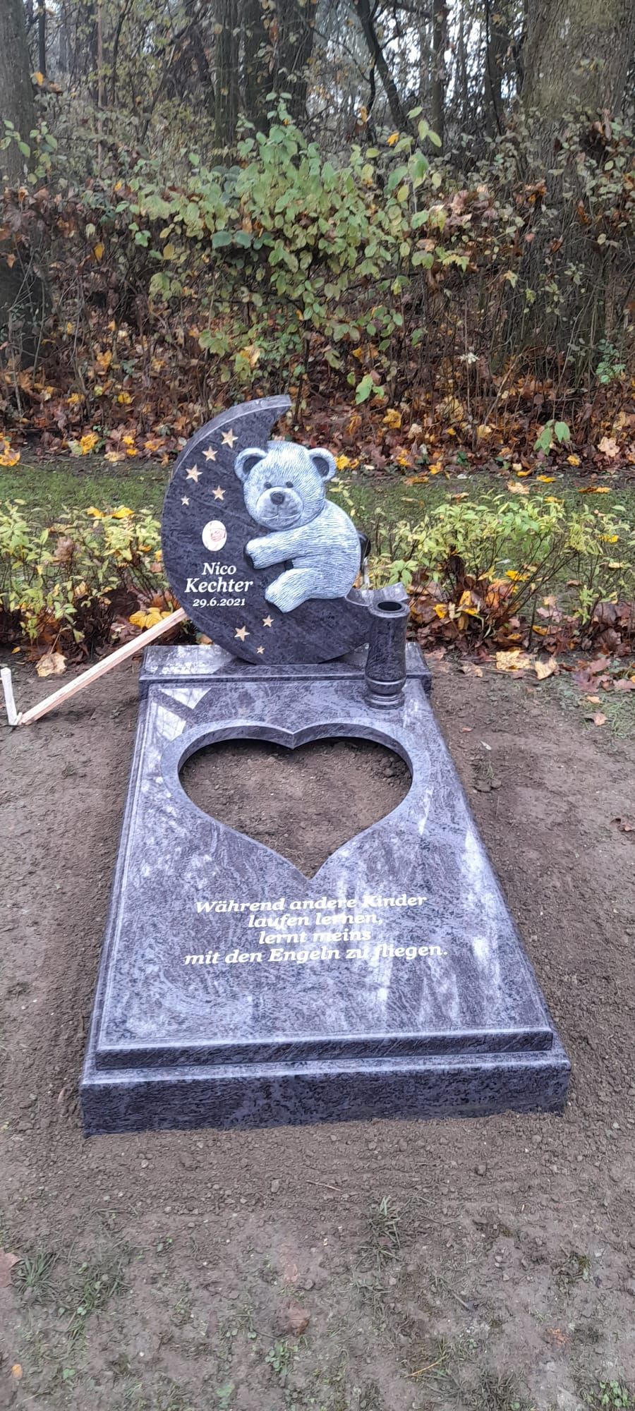 Herzförmiger Grabstein mit Teddybär- und Mondmotiv auf einem Friedhof