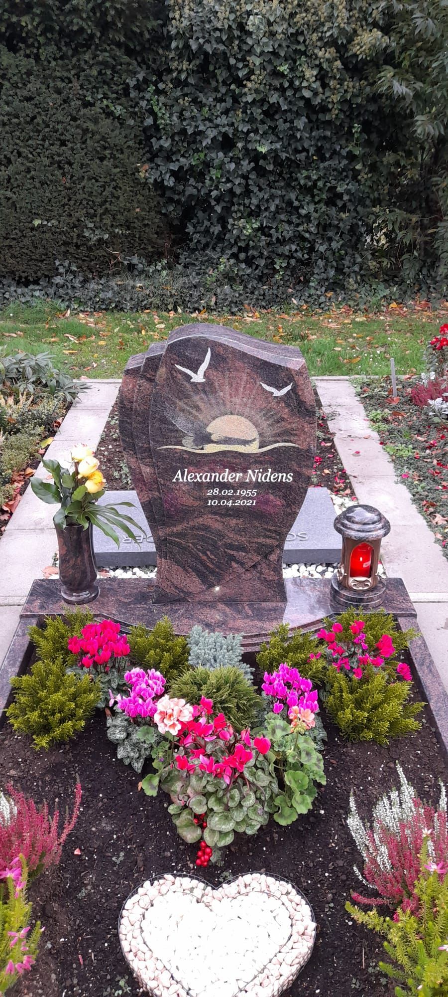 Grabstein mit Blumen und einem weißen Herzdenkmal in einer Gartenanlage