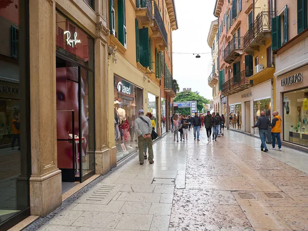 Un grupo de personas camina por una calle adoquinada frente a una tienda Ray-Ban.