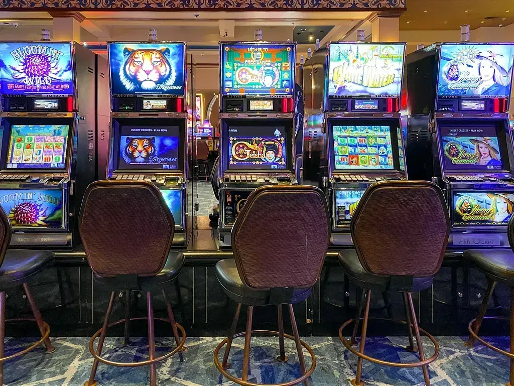 Una fila de máquinas tragamonedas en un casino con sillas delante de ellas.