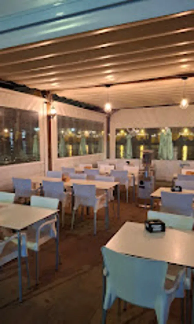 Restaurante interior con mesas y sillas blancas y paredes transparentes, ambientación nocturna.