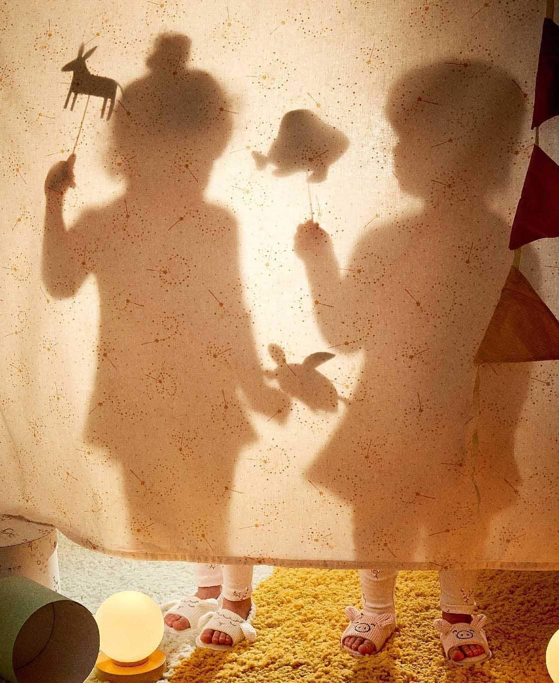 Sombras de dos niños sosteniendo marionetas de animales detrás de una sábana; juego de luces.