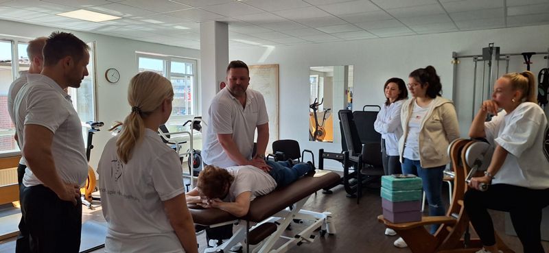 Eine Gruppe von Menschen steht in einer Turnhalle um einen Tisch herum.