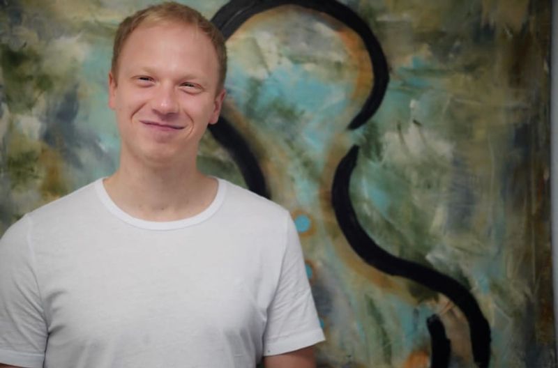 Ein Mann in einem weißen Hemd steht vor einem Gemälde.