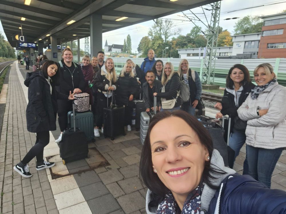 Lächelnde Gruppe von Menschen mit Gepäck auf einem Bahnsteig, die ein Selfie machen.