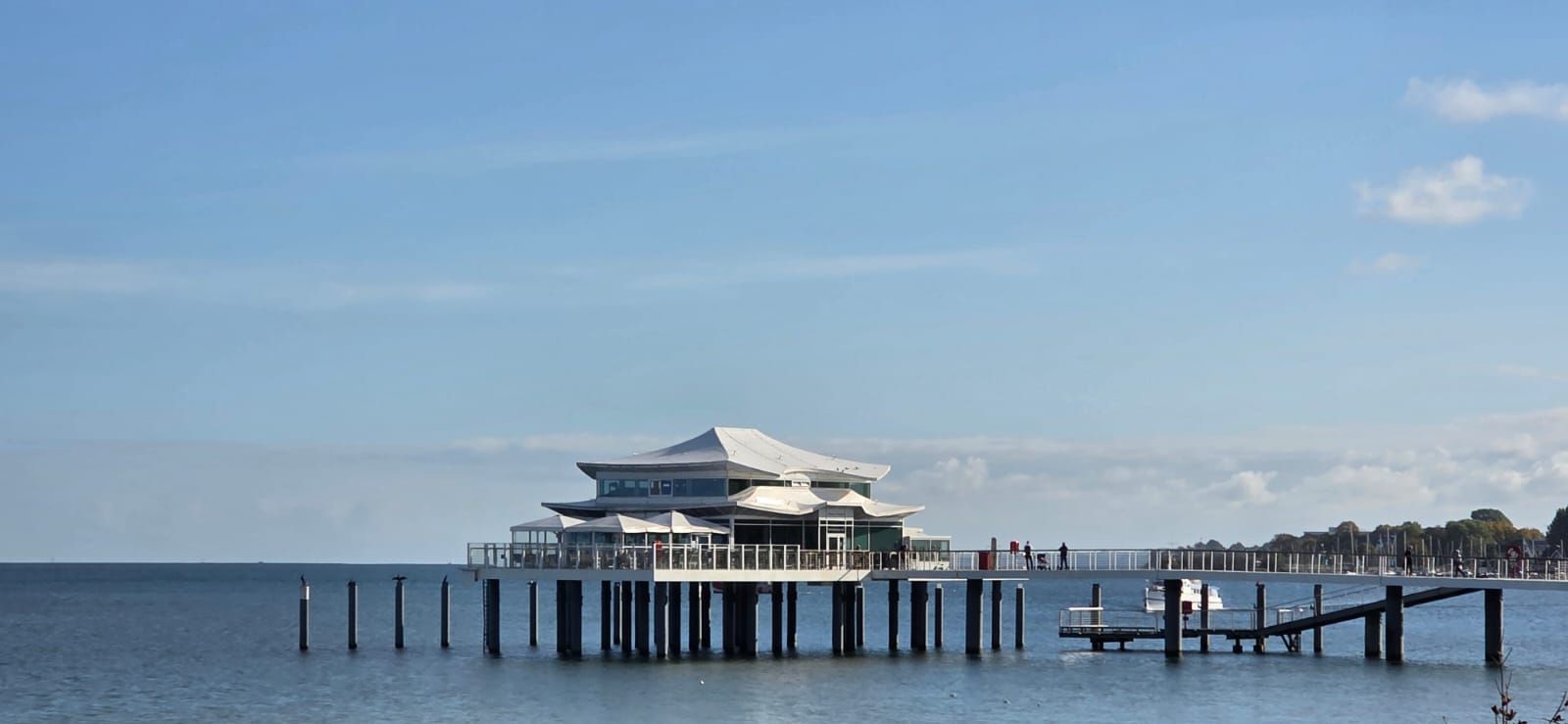 Restaurant auf Stelzen, die ins Meer ragen, mit blauem Himmel darüber.