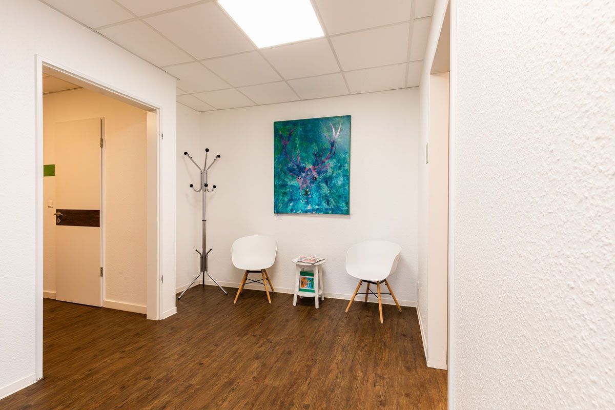 Ein Wartezimmer mit zwei Stühlen und einem Gemälde an der Wand.