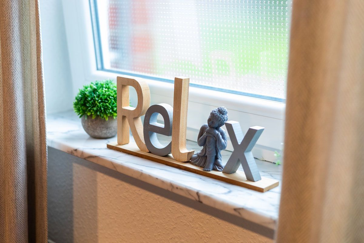Auf einem Fensterbrett steht ein Holzschild mit der Aufschrift „Entspannen Sie sich“.