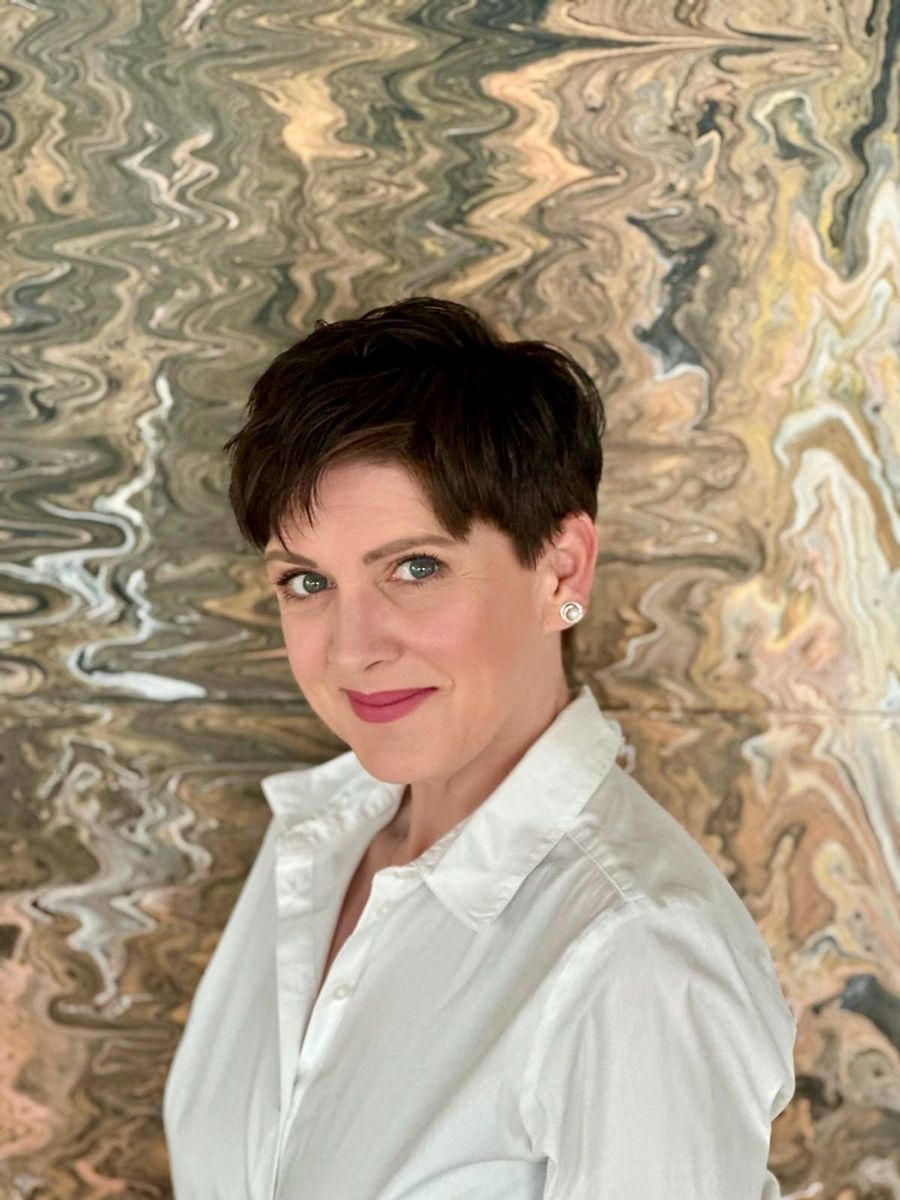 Eine Frau in einem weißen Hemd steht vor einem Gemälde.