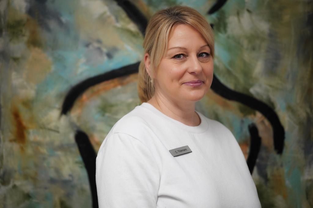 Eine Frau in einem weißen Hemd steht vor einem Gemälde.