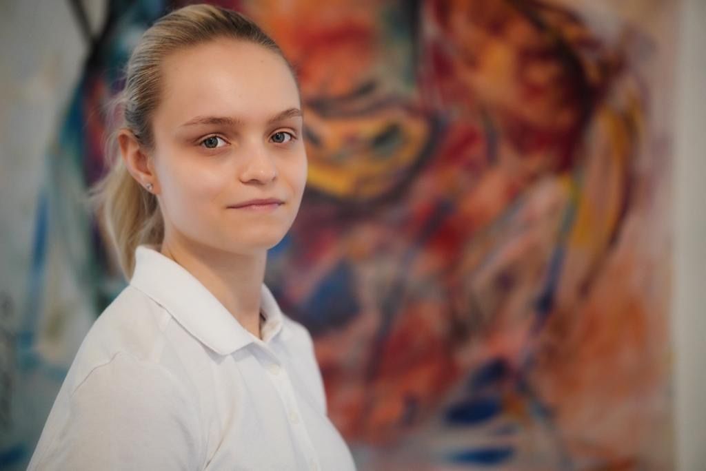 Eine Frau in einem weißen Hemd steht vor einem Gemälde.