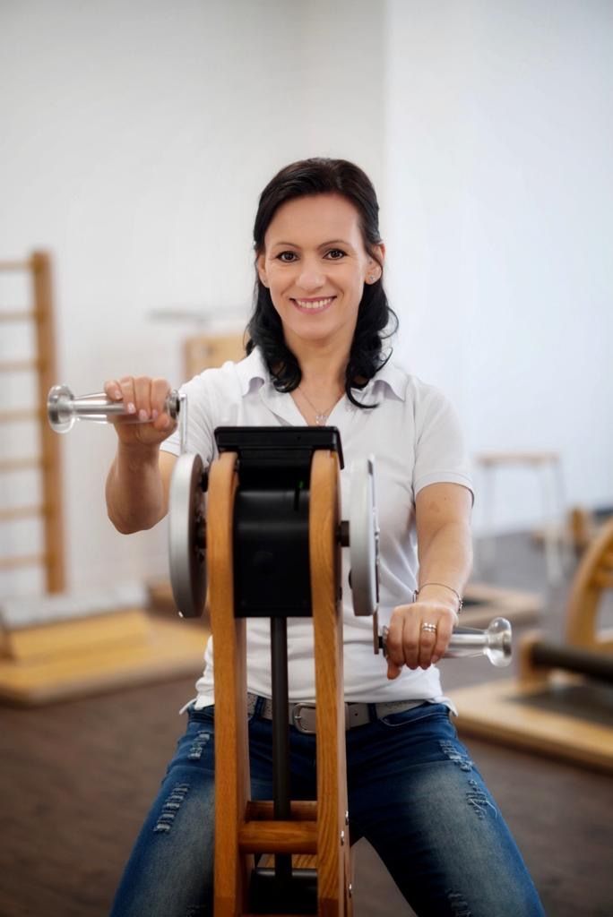 Eine Frau sitzt in einem Fitnessstudio auf einem Gerät und hält eine Hantel.