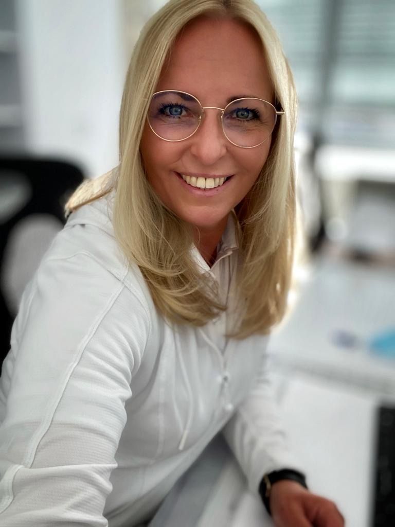 Eine Frau mit Brille und weißem Hemd lächelt in die Kamera.