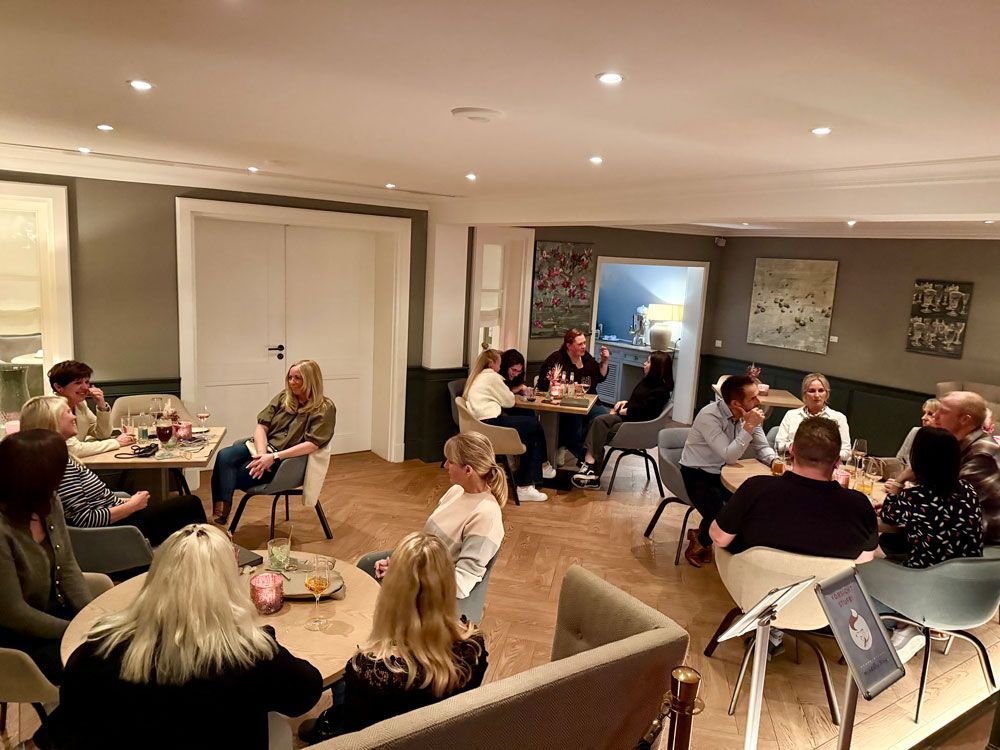 Menschen sitzen an Tischen in einem Restaurant und unterhalten sich. Gedämpftes Licht, neutrale Töne und Holzböden.