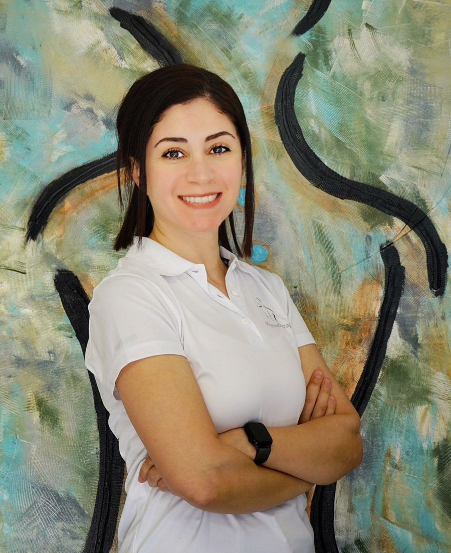 Eine Frau in einem weißen Hemd steht mit verschränkten Armen vor einem Gemälde.