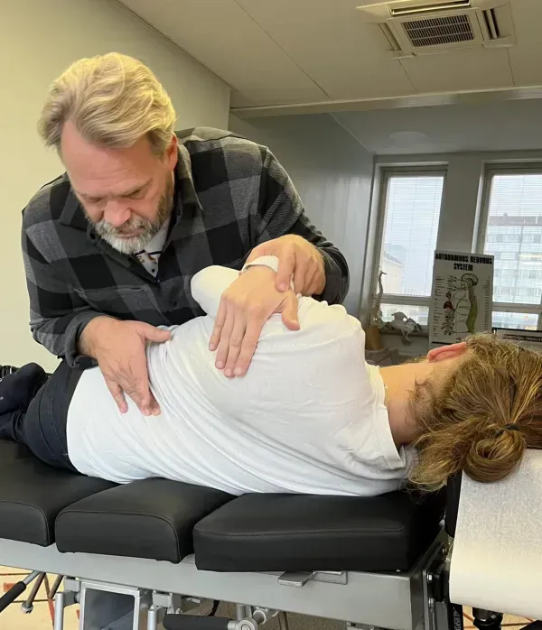 Kiropraktikko säätää kyljellään makaavaa naista hoitopöydällä klinikalla.