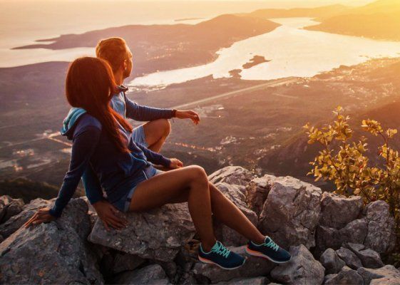 Kaksi vaeltajaa istuu kallioilla auringonlaskun aikaan ja katsoo vuorijärveä ja kaukaisia ​​huippuja.