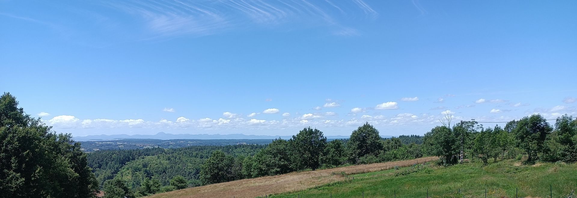 Vaste paysage pittoresque avec ciel bleu, nuages ​​épars, collines verdoyantes et horizon lointain.