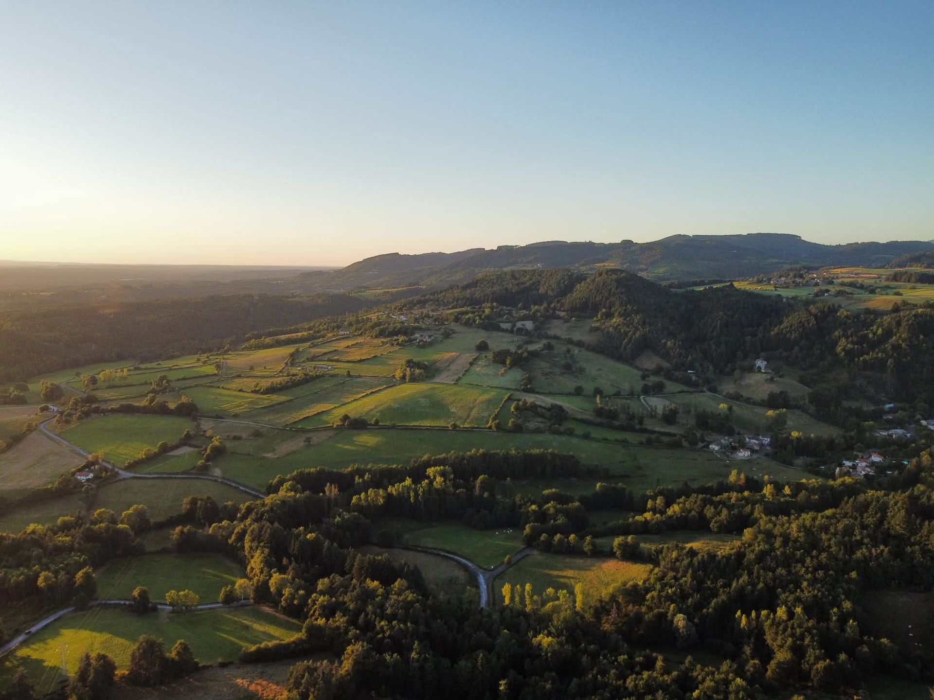 Champs en mosaïque baignés de soleil et collines verdoyantes ondulantes sous un ciel bleu limpide au lever du soleil