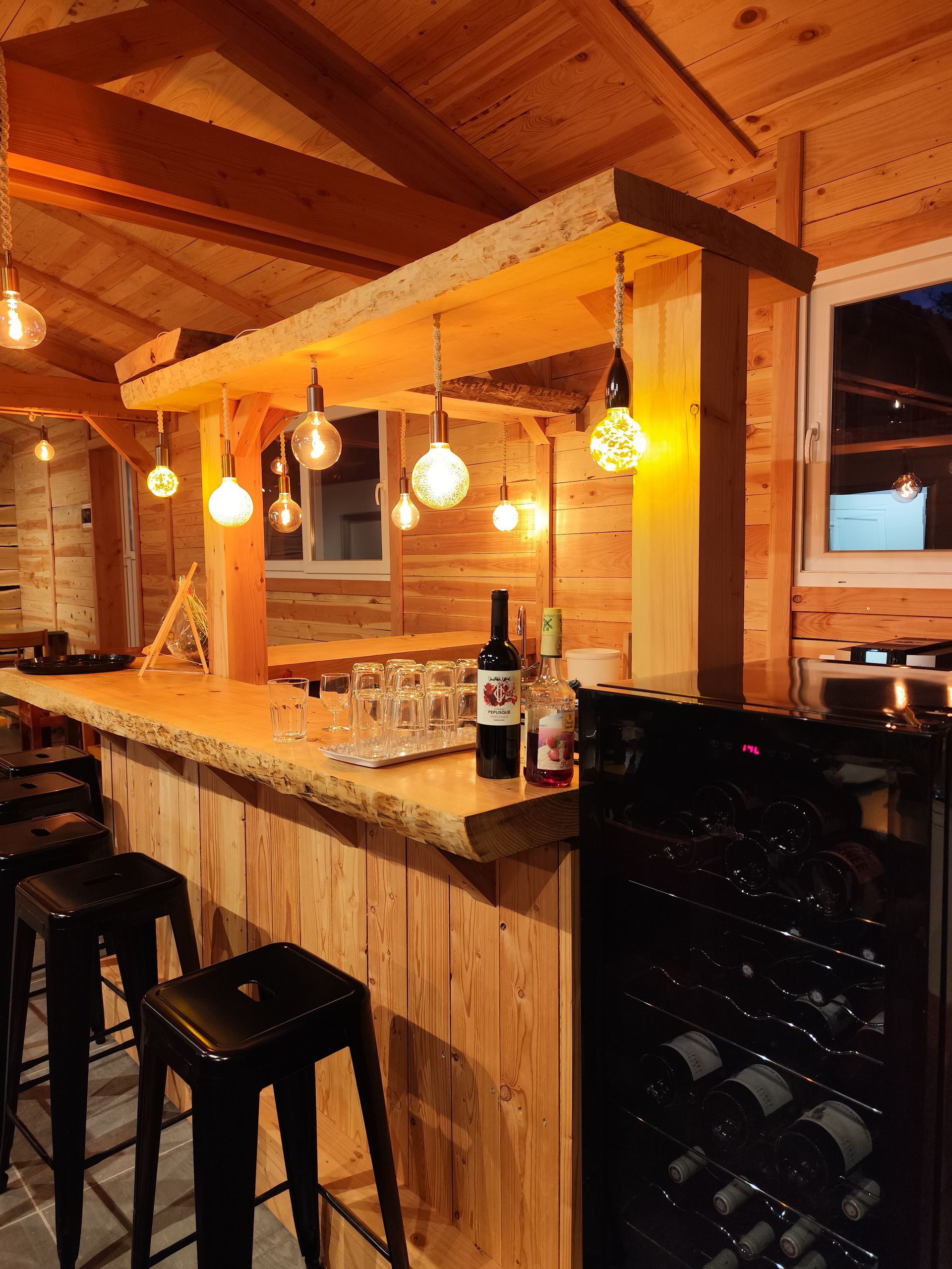 Intérieur de bar chaleureux en bois avec ampoules suspendues, tabourets et casier à vin sous une douce lumière ambrée